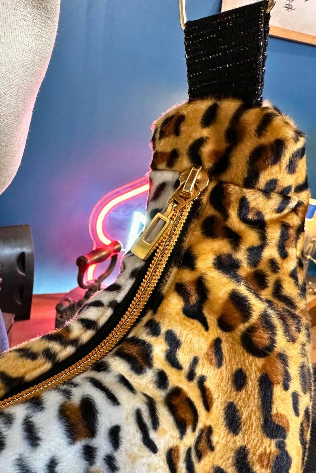 Sac à main en fausse fourrure léopard avec fermeture éclair et bandoulière, style moderne et audacieux.