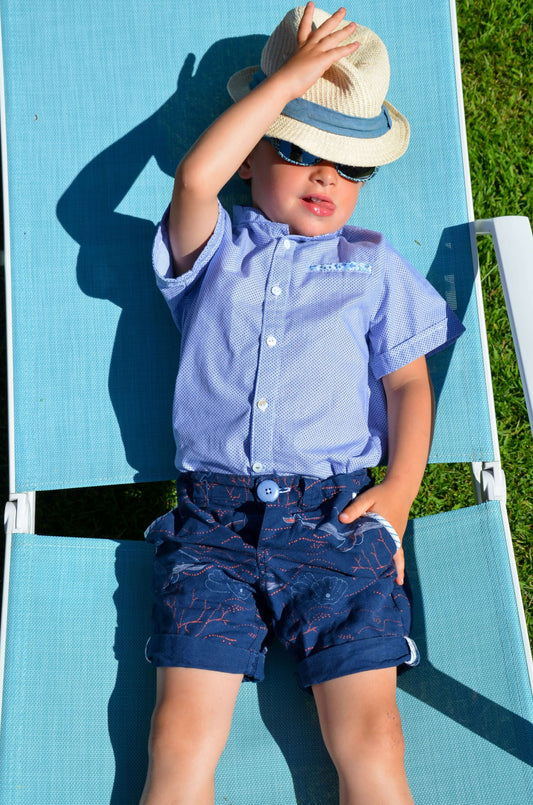 Enfant portant une chemisette et un bermuda, relaxant au soleil sur un transat, parfait pour l'été.