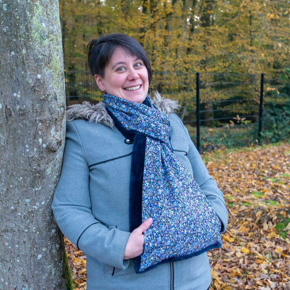 Femme souriante portant une écharpe originale Baie rose en pleine nature, avec un manchon pour les mains.