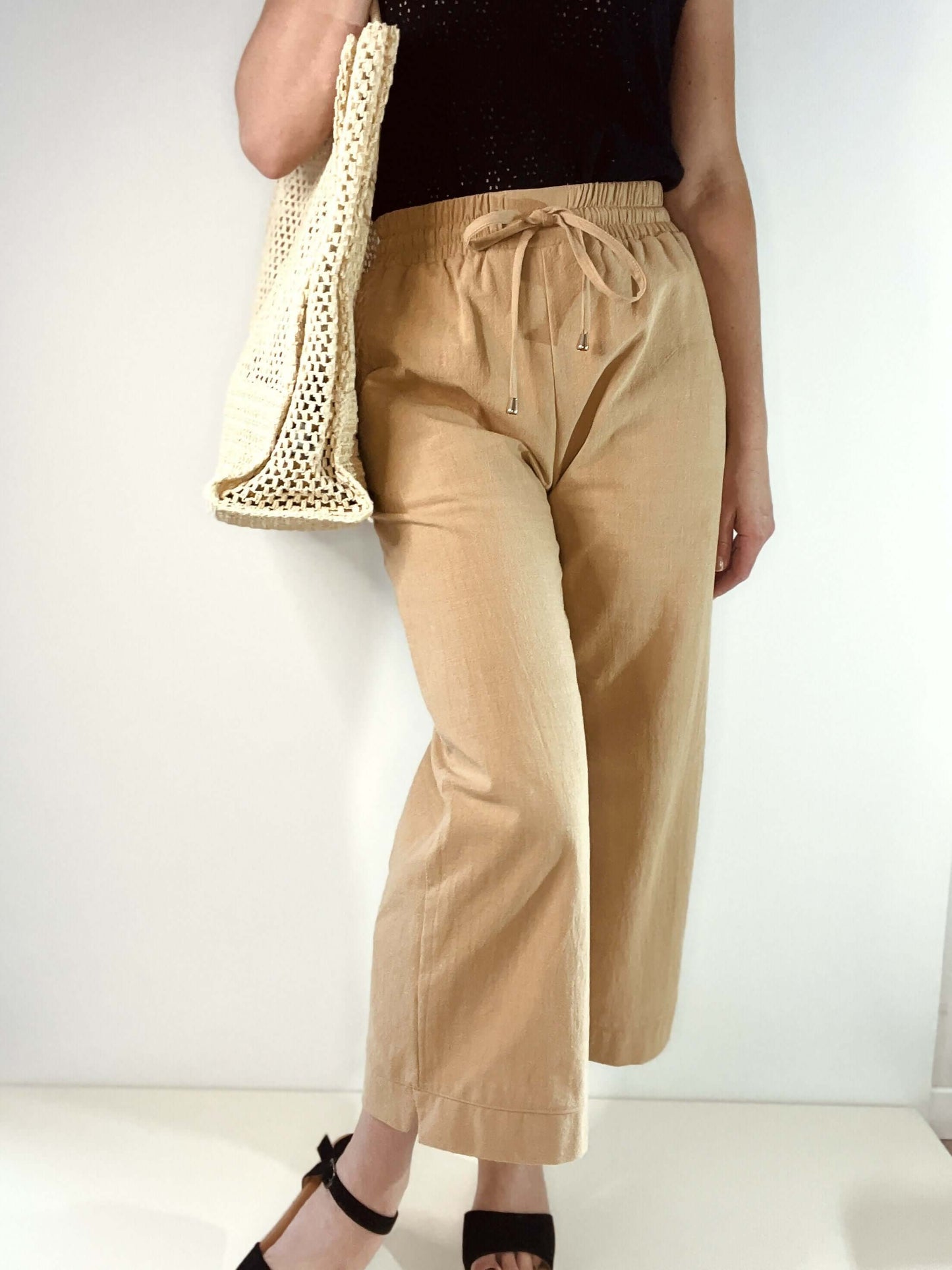 Pantalon ample beige avec taille élastique, porté avec un sac en filet, idéal pour un look décontracté.