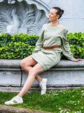 Modèle portant CACAO - LE sweat / t-shirt multi-options en vert, patron de couture pdf à télécharger, assise sur un mur en pierre.