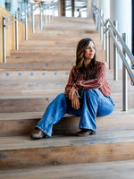 Femme assise sur des escaliers en bois portant une chemise rayée et un jean évasé dans un décor moderne.