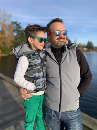Père et fils portant Duo KEZIA - Doudoune sans manches mixte au bord d'un lac, idéale pour la mi-saison, patron de couture pdf à télécharger.