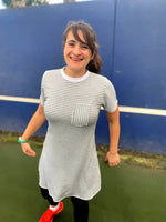 Femme souriante portant une robe rayée grise et blanche avec poche avant, sur un terrain de sport.