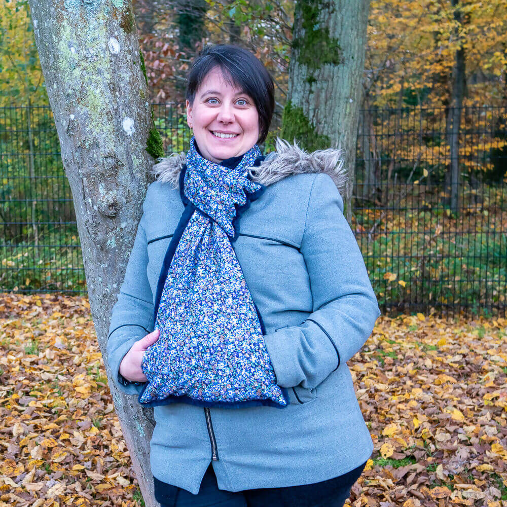 Femme souriante portant une écharpe avec manchon Baie rose, en pleine nature automnale.