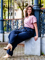 Femme portant FIGUE - La blouse parfaite, patron de couture pdf à télécharger, assise sur un banc en extérieur avec des pantalons bleu marine.