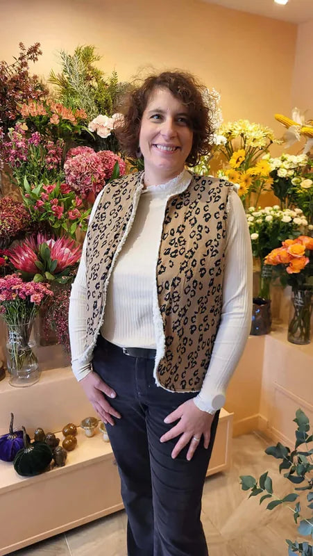 Femme portant un Gilet de Berger Cérès, devant un fond de fleurs colorées, look tendance et décontracté.