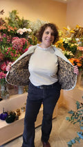 Femme dans un gilet de berger Cérès, montrant l'intérieur doublé, avec fleurs en arrière-plan.
