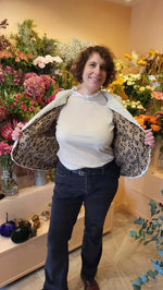 Femme dans un gilet de berger Cérès, montrant l'intérieur doublé, avec fleurs en arrière-plan.