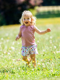 Enfant joyeuse portant un short à motif floral, courant dans un champ de fleurs. KUMQUAT - Le short / bermuda / pantalon, patron de couture pdf à télécharger.
