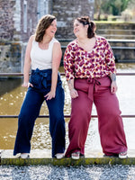 Deux femmes portant le NASHI - Le pantalon palazzo, un patron de couture PDF à télécharger, posent joyeusement sur un pont.