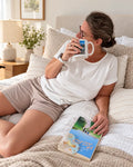 Femme portant le Patron PDF Pyjama NOVA du 34 au 60, assis sur un lit en coton blanc cassé