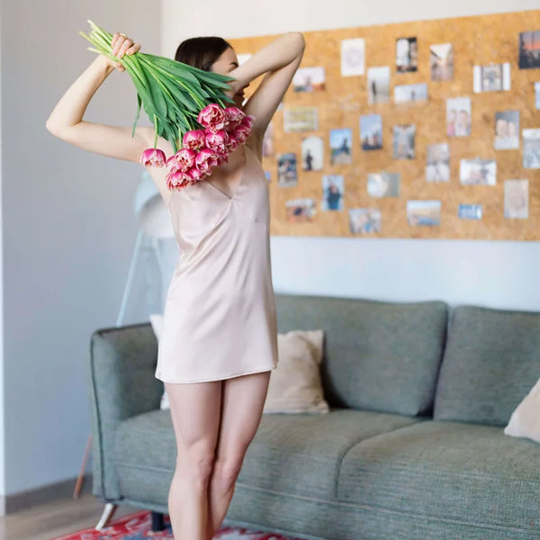 Personne tenant des fleurs portant une nuisette courte, ambiance printemps dans un salon moderne. Nuisette- XXS/L - SPRING BLOOM, patron de couture.
