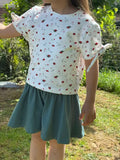 Enfant portant le Patron PDF Jupe Short LILAS & COQUELICOT, short évasé bleu-gris, t-shirt blanc motifs fleuris