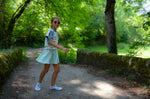 Jeune fille portant le Patron PDF Jupe Short LILAS & COQUELICOT, short bleu ciel, sur un chemin forestier ombragé