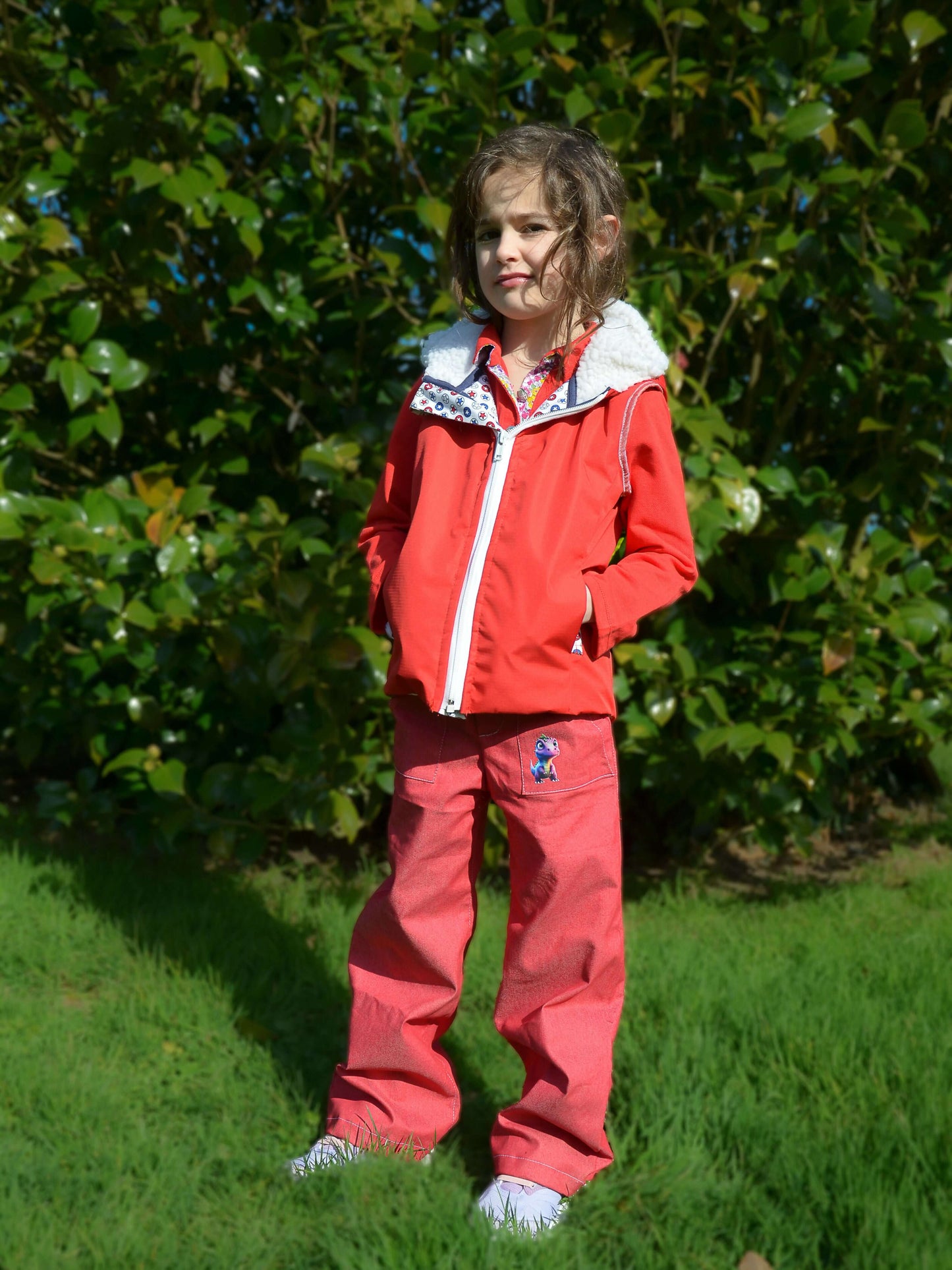 Fille portant un Pantalon BAGGY ALVIDA rouge devant des buissons, parfait pour patron de couture pdf à télécharger.