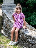 Enfant portant le Patron PDF AMARENA, robe courte à fleurs roses et mauves, assise sur un muret de pierre