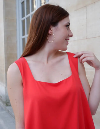 Femme portant le Patron PDF Débardeur Manille du 32 au 48, vue de profil en rouge, devant un mur de pierre