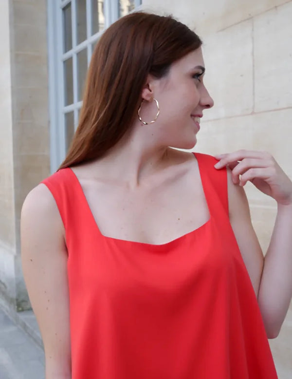 Femme portant le Patron PDF Débardeur Manille du 32 au 48, vue de profil en rouge, devant un mur de pierre