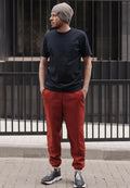 Homme portant le Patron PDF Comfortino, pantalon rouge et t-shirt noir, bonnet gris, devant portail métallique
