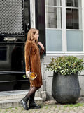 Femme portant le Patron PDF Robe Zoya en velours côtelé marron, devant une porte noire