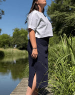Femme portant le Patron PDF Robe et Top Cotelle, jupe midi fendue en coton bleu marine, top blanc, au bord de l'eau