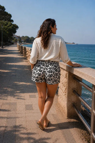 Femme portant le Patron PDF Short Figuette du 34 au 54 en motif floral noir et blanc, vue de dos au bord de mer