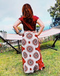 Femme portant une jupe longue imprimée rouge avec motifs circulaires devant un hamac dans le jardin.
