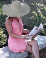 Femme portant une Robe Hécate - T36 à 50, décolleté plongeant, lisant dehors sous un chapeau, patron de couture pdf à télécharger.