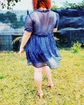 Femme portant une robe babydoll en dentelle bleu, vue de dos, dans un jardin verdoyant.