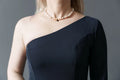 Femme portant une robe noire à une manche avec un collier de perles