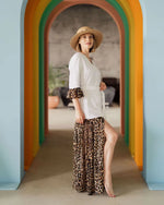 Femme portant une robe "Robe - XXS/XL - BOHEMA" avec un motif léopard, debout sous un arc en ciel coloré. Patron de couture PDF à télécharger.