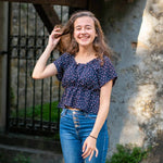Jeune femme souriante en haut à motifs devant une porte en pierre
