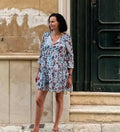 Femme portant une robe légère avec motif, ajustée à la taille, style Sorolla, devant un mur. Patron de couture pdf à télécharger disponible.