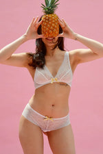 Femme portant le Soutien-gorge Smoothie en dentelle, tenant un ananas devant un fond rose. Patron de couture PDF à télécharger.