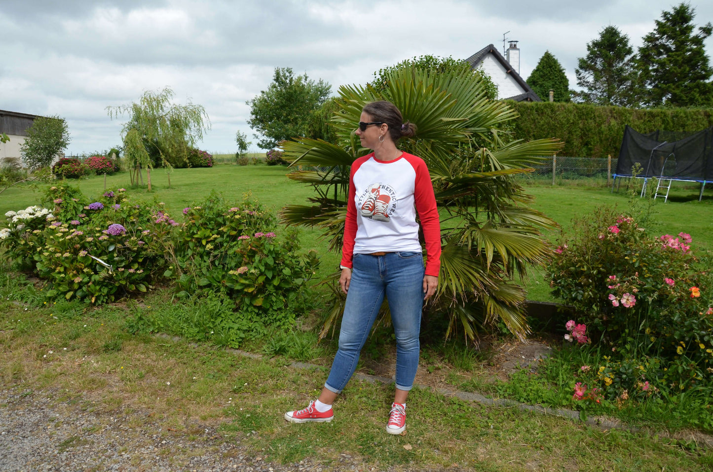 Femme portant un T-shirt à manches raglan rouge, dans un jardin verdoyant, style décontracté.