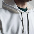 Gros plan d'un sweat à capuche blanc porté par un homme, cordons de couleur sombre visibles.