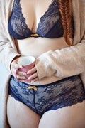 Femme en lingerie dentelle navy avec tasse rose, mettant en avant le tanga et boxer Papaya en designs confortables.
