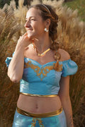 Femme portant un haut bleu avec détails dorés, fond nature. Top Yasmine Femme - Patron couture du 32 au 56. Patron de couture PDF à télécharger.