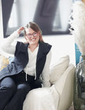 Femme souriante portant la veste Bogota, confortablement assise dans un intérieur élégant, mettant en valeur la couture et le style.