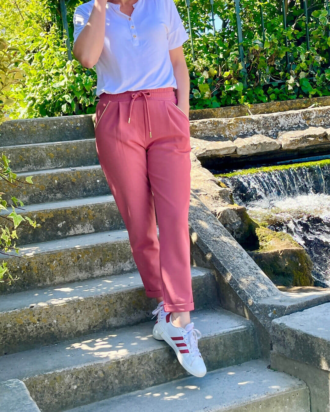 Femme portant le pantalon Sprint rose, confortable et élégant, en marchant sur des escaliers au bord d'un ruisseau.