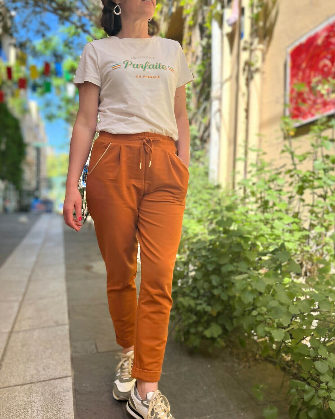 Femme portant le pantalon Sprint orange avec un t-shirt dans une rue, idéal pour un look sportif et élégant.