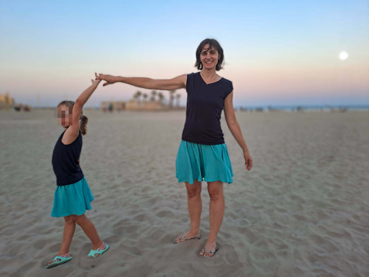 Mère et fille à la plage, vêtues de jupes courtes colorées, s'amusant ensemble au coucher du soleil.