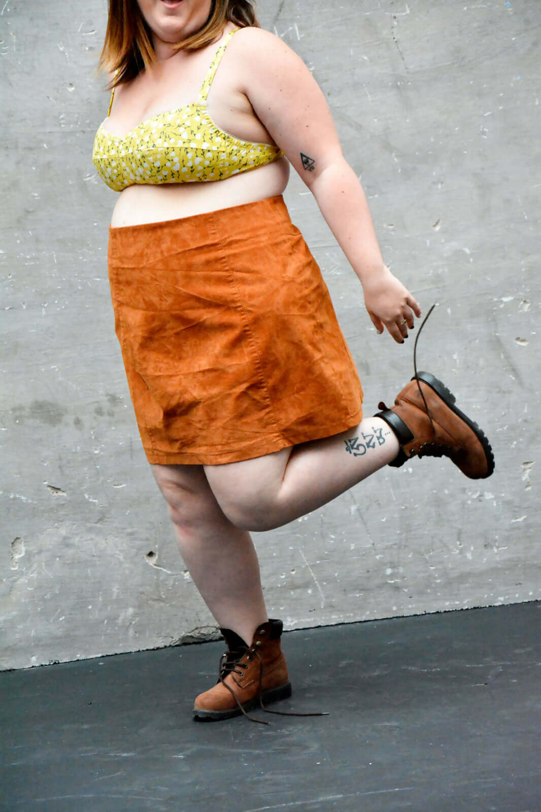 Femme portant une brassière jaune et une jupe orange, affichant un style décontracté avec des bottes.