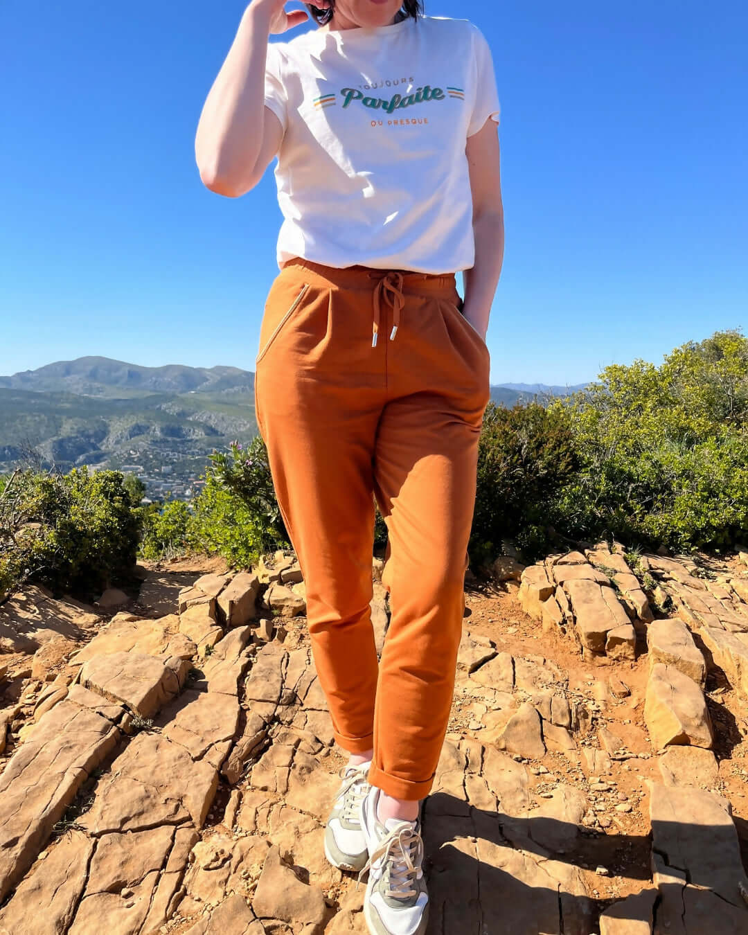 Femme portant le pantalon Sprint orange et un t-shirt, posant en plein air avec des montagnes en arrière-plan.