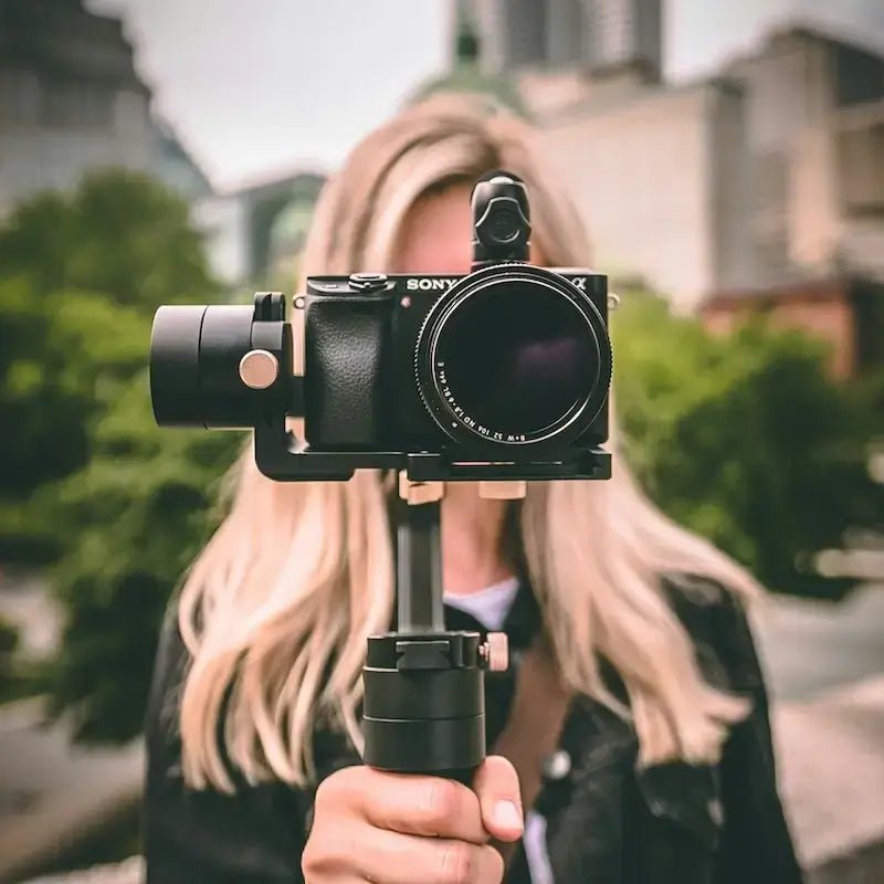 Personne tenant un appareil photo moderne dans un cadre urbain flou, prêt à capturer des moments uniques.