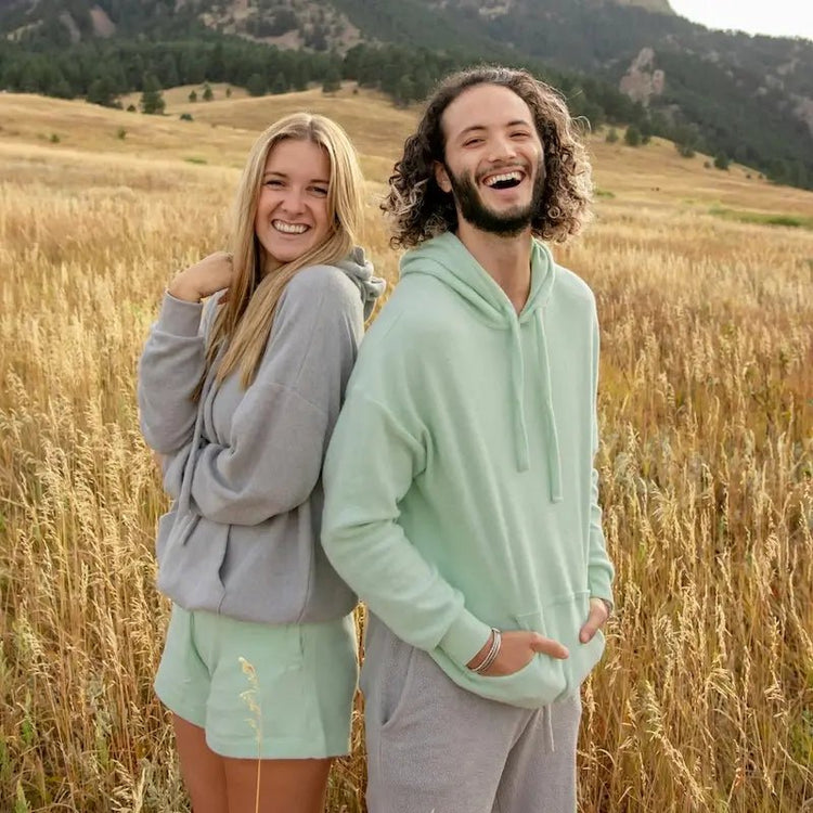 Couple souriant portant des sweats dans un champ, illustrant la collection de Patrons de Sweats