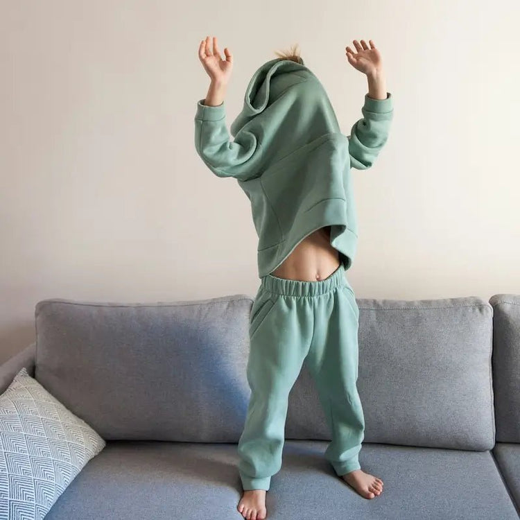 Enfant portant un sweat vert pastel sur un canapé, illustrant les Patrons de Sweats Enfant de la collection de patrons de couture PDF à télécharger.