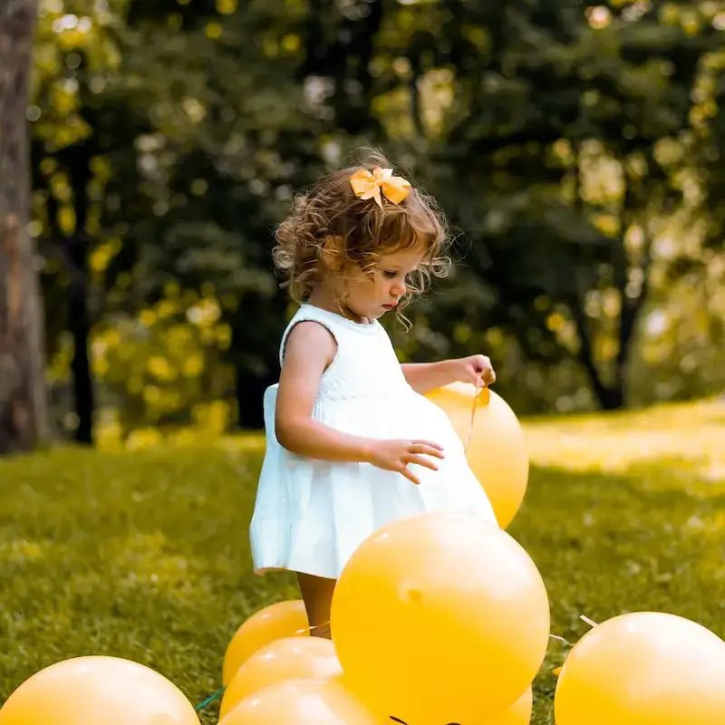 Petite fille en robe blanche avec des ballons jaunes, illustrant les Patrons pour Enfant, collection de patrons de couture pdf à télécharger.