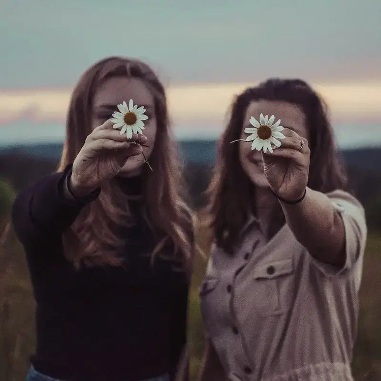 Deux femmes tenant des marguerites au crépuscule, symbolisant la liberté et la nature.